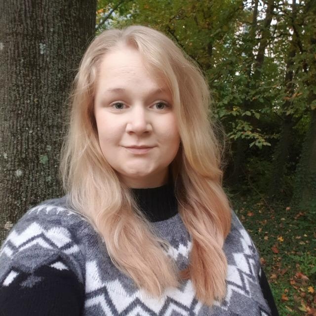 Portrait of a young woman with long blonde hair, wearing a patterned sweater, outdoors in autumn.